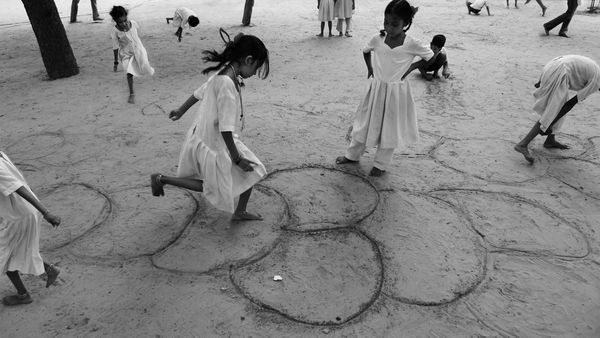 Children hard at work playing in the sand. Some play hopscotch, some draw things, some observe. Are these political acts?