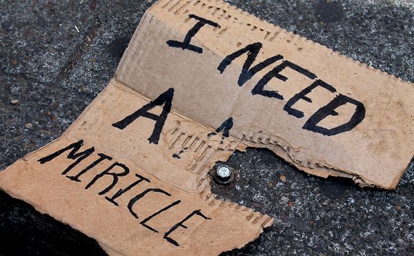 A cardboard sign, reading "I NEED A MIRICLE," has seen better days. It's ripped and lying on concrete, abandoned.